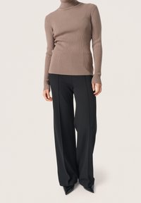 Maglione marrone a coste con collo alto abbinato a pantaloni neri a gamba larga e vita alta, e décolleté nere con punta affilata. Texture lisce, design aderente.