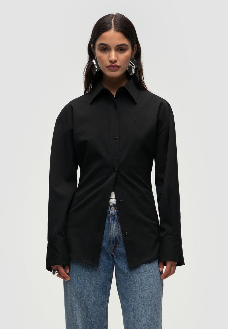 Sort langærmet skjorte med knaplukning foran, der har en klassisk krave og subtil logo-brodering, parret med lyseblå jeans.
