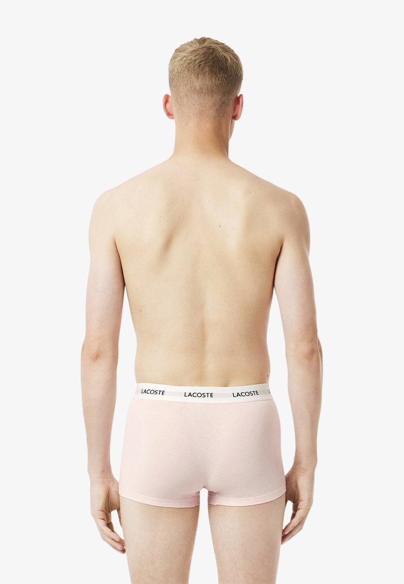 Rosa Baumwoll-Boxershorts mit einem schwarz-weißen Lacoste-Logo auf dem elastischen Bund, von hinten gezeigt, glatte Textur, figurschmeichelndes Design.
