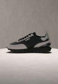 Μαύρο και γκρι χαμηλό παπούτσι με μαύρα κορδόνια, υφή σόλας και το λογότυπο "ICEBERG" στο πλάι, εκτεθειμένο σε ανοιχτή επιφάνεια με γκρι φόντο.