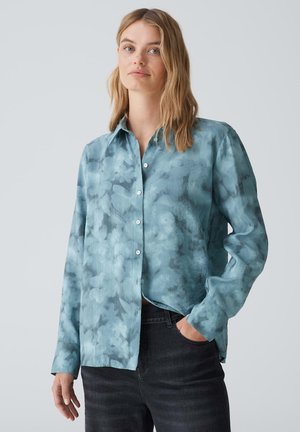 Camicia azzurra chiaro, con bottoni, realizzata in un tessuto morbido con un motivo acquerellato. Presenta maniche lunghe e un colletto classico.