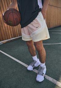 Nike basketo šortai su šviesiai rožine ir geltona dizainu, turintys šoninius kišenes ir juodą logotipą, derinami su pilkais sportbačiais ir baltais kojinaitėmis.