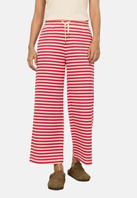 Pantalons larges à rayures rouges et blanches avec une taille élastique et un cordon de serrage. Le tissu semble doux et léger. Portés avec des sabots marron.