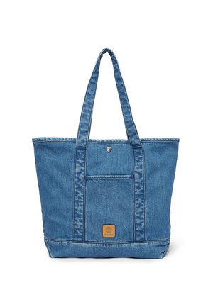 Sac fourre-tout en denim bleu avec longues anses, poche avant sécurisée par un bouton pression en métal, et petite étiquette de marque en cuir sous la poche.