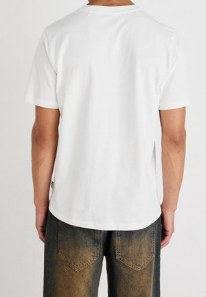 Witte katoenen T-shirt met een ronde hals, korte mouwen en een rechte zoom. Draagt met vervaagde blauwe spijkerbroek met achterzakken.