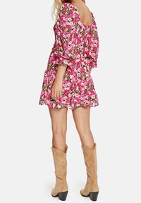 Blumiges Minikleid mit Puffärmel, das in pinken, roten und grünen Mustern gestaltet ist. Strukturierter Stoff, kombiniert mit tanfarbenen, kniehohen Stiefeln.
