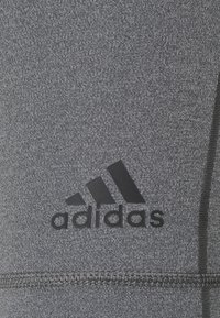 Tela atlética gris con una superficie texturizada, que presenta un logo de Adidas en negro. Incluye costuras decorativas en el lateral.