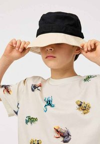 Sort og beige bøttehat med bred skygge, båret af et barn. T-shirten har farverige frø-tryk på en lys baggrund.