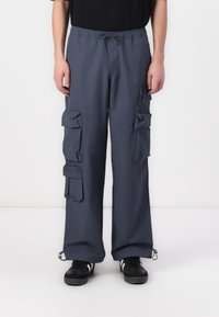 Navy cargo trousers with elastic waistband, multiple flap pockets, and drawstring hems. Made from lightweight fabric, featuring a relaxed fit.