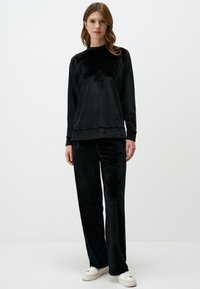 Set di abbigliamento da casa in velluto nero composto da una maglia a maniche lunghe con scollo rotondo e pantaloni dritti, entrambi con una texture liscia e morbida.