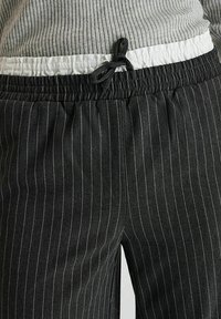 Pantalons à rayures noires avec une finition texturée ; taille élastique avec un accent blanc et cordon de serrage réglable.