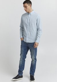 Lys blå, stripete skjorte med lange ermer, paret med falmede blå jeans og svarte joggesko. Enkelt bakgrunn, ingen tilleggdetaljer.
