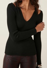 Czarna, prążkowana bluzka z długim rękawem, z dekoltem w kształcie litery V i odkrytymi ramionami. Posiada fakturowany materiał z delikatnymi liniami oraz dopasowaną sylwetkę.
