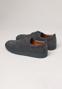 Chaussures en daim grises avec un bout arrondi, laçage à six œillets, intérieur en cuir et semelle en caoutchouc. Détail de surpiqûre discrète sur l'empeigne.