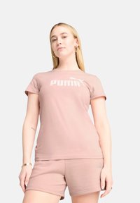 Šviesiai rožinė medvilnės marškinėliai trumpomis rankovėmis ir apvaliu iškirpimu. Pabrėžia didelį baltą "PUMA" logotipą per krūtinę ryškiu šriftu.