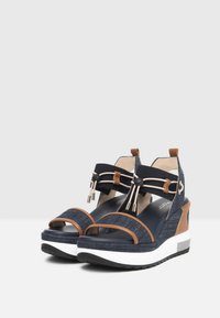 Keil-Sandalette in Jeansblau mit Tan-Akzenten, zwei vorderen Riemen, einem Stoffknöchelband und einer weißen Sohle mit strukturiertem Griff.