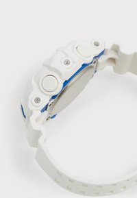 Montre numérique blanche et bleue avec un boîtier texturé, trois boutons-poussoirs et un bracelet flexible à motif.
