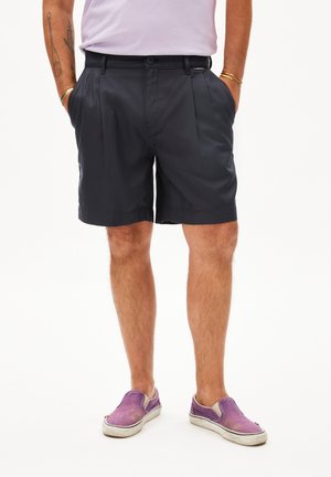 Zwarte marineblauwe geplooide shorts van lichtgewicht stof, met zijzakken en een nette tailleband. G gedragen met paarse instap shoes.