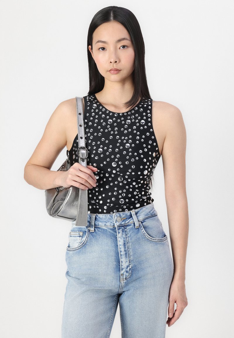 Schwarz ärmelloses Top mit silbernen Verzierungen, kombiniert mit hochgeschnittenen hellblauen Jeans und einer kleinen silbernen Handtasche. Glatte Textur.