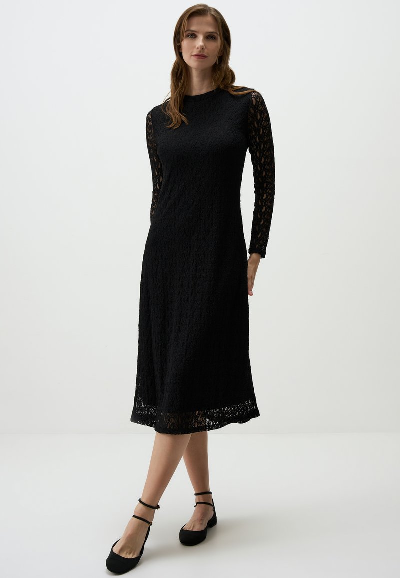 Schwarzes Spitzenkleid mit langen, durchsichtigen Spitzenärmeln, rundem Halsausschnitt und ausgestelltem Schnitt. Abgerundet mit einem gewellten Saum.