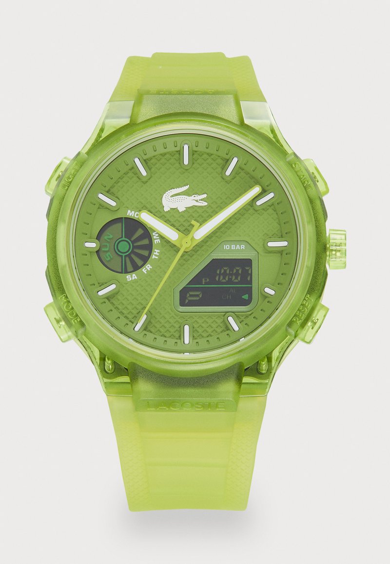 Grønn digital klokke med gjennomsiktig gummirem, teksturert urskive, hvite detaljer og digital skjerm. Har Lacoste-logo og flere urskiver.