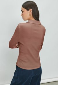 Camicia a maniche lunghe con colletto in rosa polveroso. Tessuto liscio, design aderente, tessuto a coste. Abbinata a pantaloni scuri e larghi.
