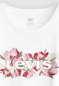 Λευκό βαμβακερό t-shirt με λουλουδάτο σχέδιο σε ροζ και πράσινο, με το κείμενο "Levi's" σε έντονη λευκή γραμματοσειρά πάνω σε φόντο με φυτά.