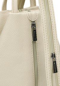 Krémová kožená kabelka s texturovaným povrchem, horními uchy a dvojitými zipy, které mají stříbrné kování a detaily s logem.