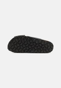 Svarte sko med teksturert såle som har sirkulære mønstre. Glatt overdel med en lett bue. Fokuserer på minimalistisk stil.