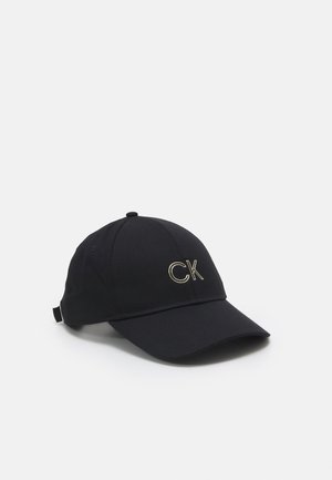 Casquette de baseball noire avec visière courbée et sangle réglable, arborant un logo "CK" doré brodé sur le panneau avant.