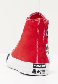 Sneaker alta rossa in tela con suola in gomma bianca, cuciture a contrasto e un piccolo patch logo nero e bianco sul tallone.