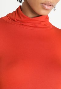 Röd polotröja i mjukt, stretchy tyg; har en hög krage och sitter nära kroppen med en fin ribbad textur.