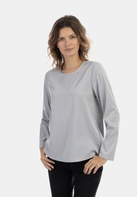 Világosszürke, hosszú ujjú blúz, kerek kivágással, sima textúrával és lazán illeszkedő fazonnal. Fekete nadrággal párosítva, semleges háttér előtt.
