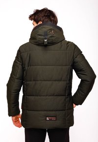 Grön puffjacka med hög krage, quiltat mönster och justerbar huva. Har en logotyp på den nedre delen av ryggen och textil med struktur.