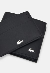 Black leather wallet featuring four card slots, a textured surface, and silver logo accents. Slim design, with clean edges and stitching.