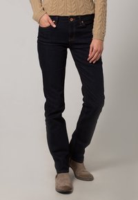 Jeans de mezclilla azul oscuro con corte ajustado, que cuentan con cinco bolsillos, un cierre frontal con botón y detalles en costura clara. Textura suave.