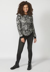 Czarny i biały sweter w wzory z teksturowanym zdobieniem, w połączeniu z czarnymi obcisłymi dżinsami i czarnymi sznurowanymi botkami do kostek.