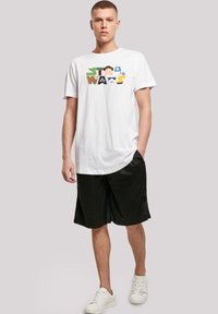 Hvit bomulls T-skjorte med et fargerikt "Star Wars"-grafikk, parret med svarte treningsshorts og hvite joggesko.