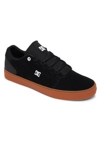 Schwarzer Wildledersneaker mit einer Gummisohle. Verfügt über drei schwarze Schnürsenkel und ein weißes Logo auf der Zunge und der Seite. Niedriges Profil.