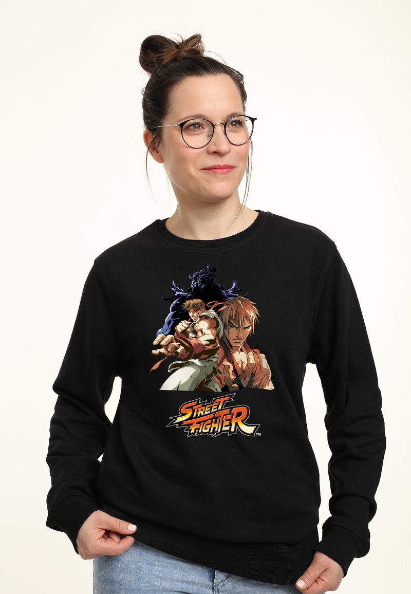 Felpa nera con stampa grafica colorata di due personaggi di Street Fighter, con un logo in caratteri audaci nella parte inferiore. Tessuto morbido.