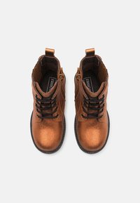 Botas de tobillo de cuero metálico marrón con cordones negros, acentos texturizados y asas de tirón en el cuello. Suelas de goma planas.