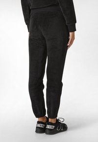 Schwarze Jogginghose aus weichem Fleece-Material, mit elastischen Bündchen und glatter Textur. Kombiniert mit schwarzen Sneakers mit weißen Akzenten.