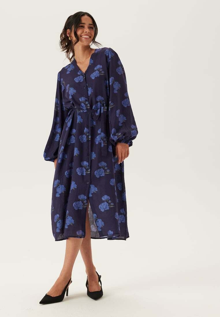 Mörkblå blommig klänning med långa ärmar, knäppning fram, skärp i midjan och midi-längd med slits detalj. Lättviktigt tyg.