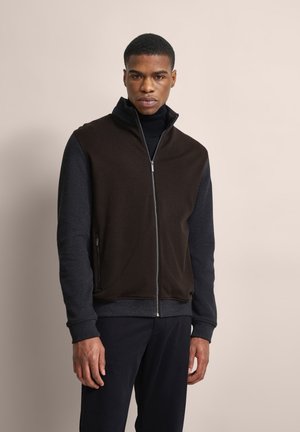 Zip-up jacket with a brown, textured front and dark grey sleeves. Boasts a high collar and side zip pockets. Smooth fabric finish.
