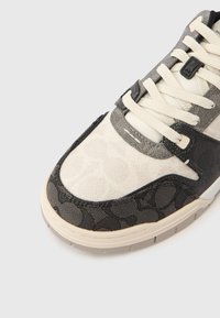 Αθλητικό παπούτσι που συνδυάζει λείες εκρού και υφασμάτινες σκούρο γκρι υλικά, με κορδόνια και μοτίβο στην περιοχή των δακτύλων. Επίπεδη σόλα από καουτσούκ.