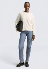 Valkoinen pörröinen neulepusero, jossa pitkät hihat, yhdistetty vaaleansinisiin suoriin farkkuihin ja mustiin korotettuihin kenkiin. Malli pitää mustaa laukkua.