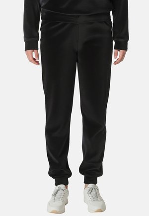 Zwarte polyester joggingbroek met een gladde textuur, elastische tailleband en taps toelopende pijpen, gecombineerd met witte sneakers. Geen patronen of accenten zichtbaar.