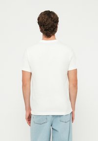 Biele bavlnené tričko s krátkymi rukávmi, okrúhlym výstrihom a voľným strihom. Zadná časť je hladká bez viditeľných log alebo vzorov.