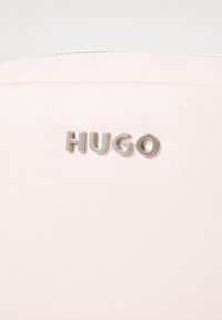 Borsa in pelle testurizzata rosa chiaro con un logo "HUGO" argento sul davanti. Il design è minimalista con linee pulite.