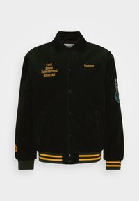 Czarna kurtka sztruksowa z żółtym haftowanym napisem i logo, zapinana na zatrzaski, z ściągaczami na mankietach oraz detalicznym haftem na rękawie.